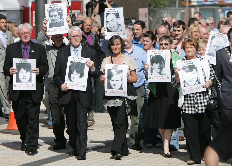 A crowd of people marching, led by eight people holding black and white photos of their loved ones who were killed.