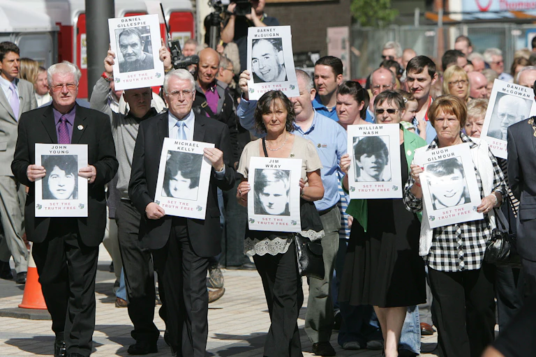A crowd of people marching, led by eight people holding black and white photos of their loved ones who were killed.