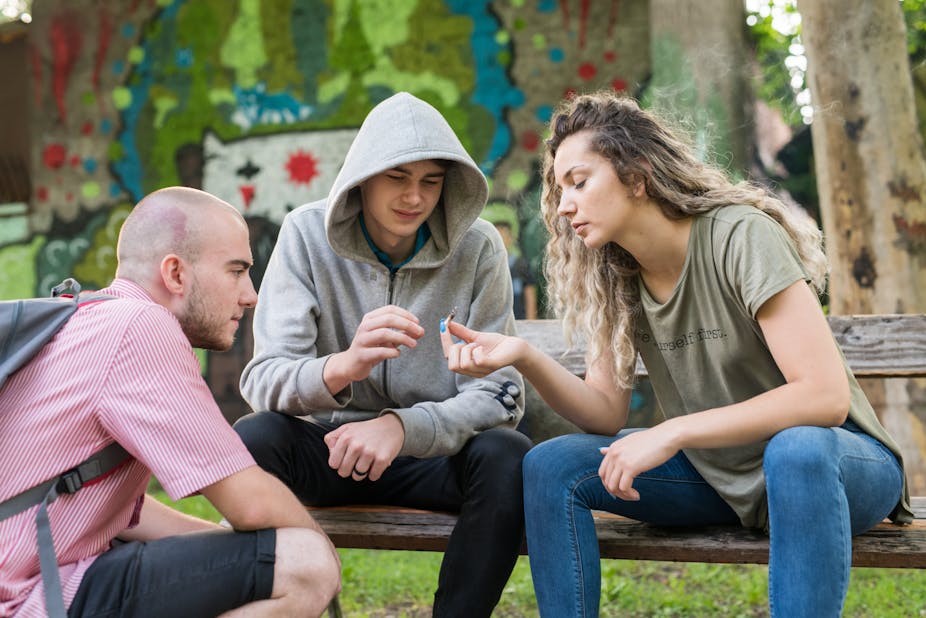 A group of three young people pass around a marijuana cigarette.