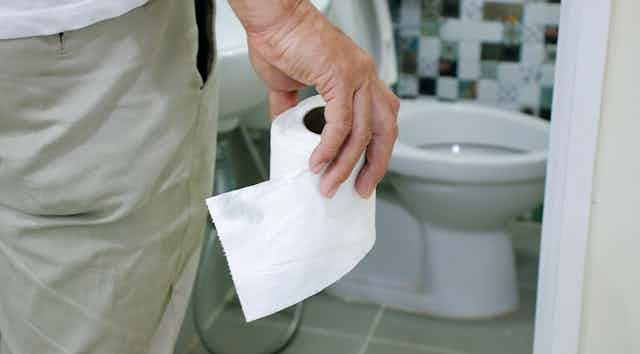 Man holding toilet paper roll approaches a toilet