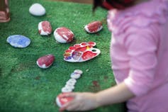 A child's hands are seen painting rocks.