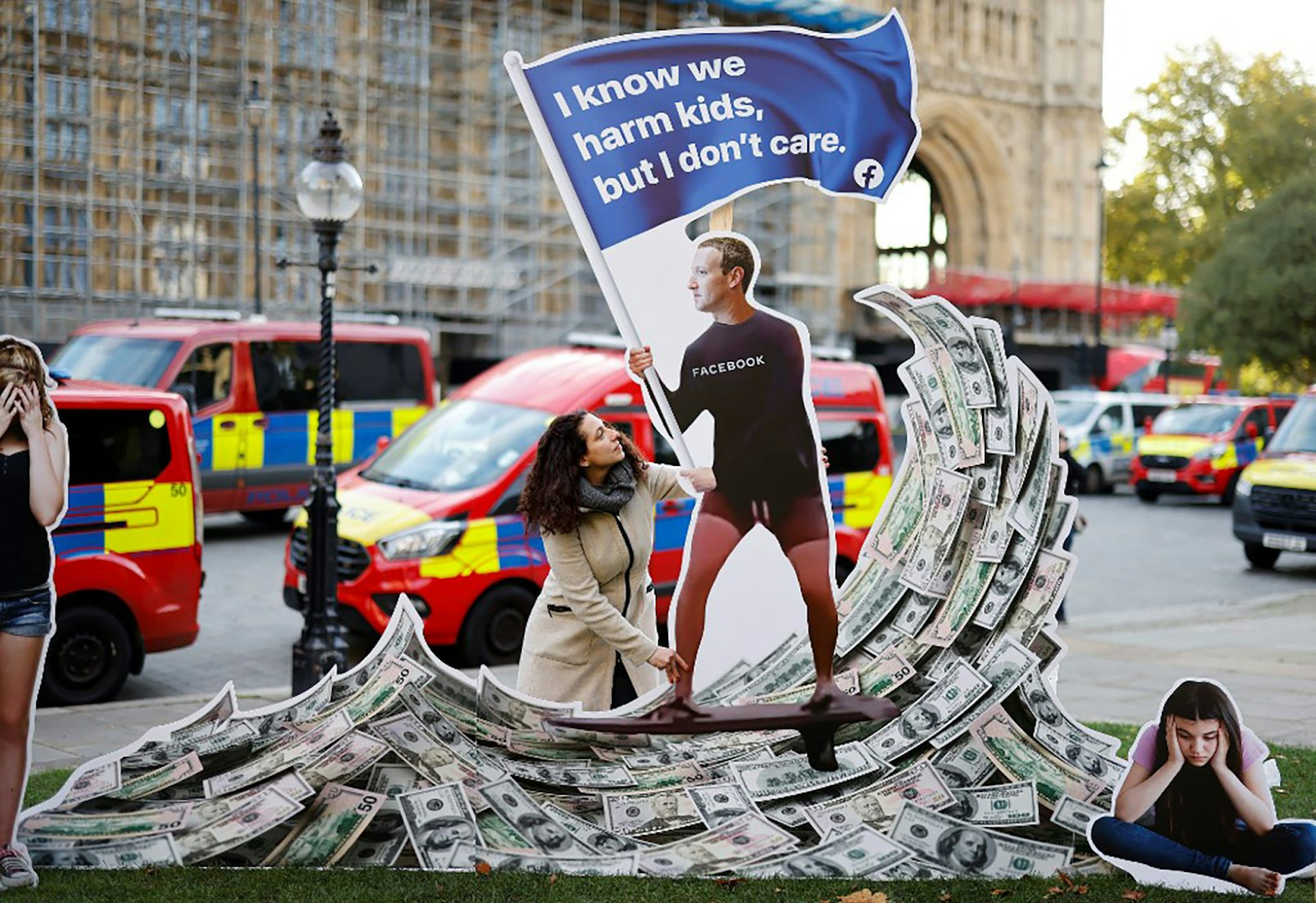 Une manifestante pose avec une installation représentant Mark Zuckerberg surfant sur une vague d’argent
