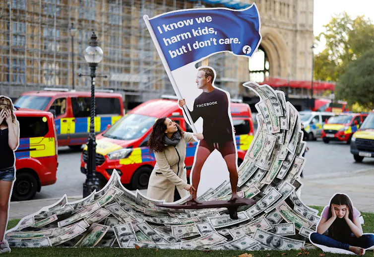 Une manifestante pose avec une installation représentant Mark Zuckerberg surfant sur une vague d’argent