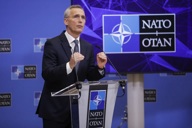 Man in suit speaks at podium in front of 'NATO' sign