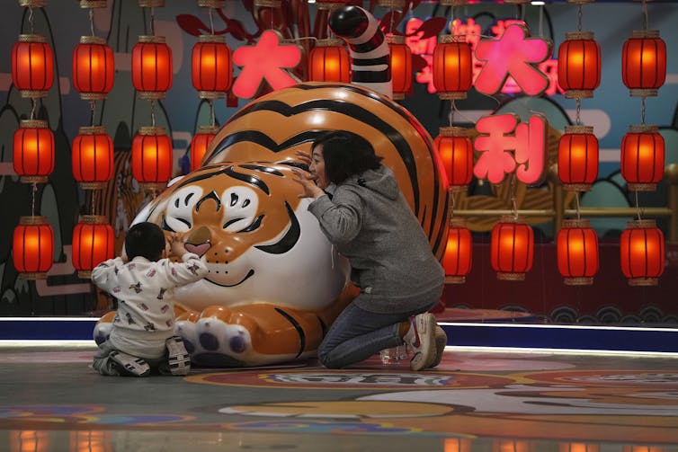 A woman and a child play on a tiger decoration they are both crouched, pretending to claw and growl at each other.