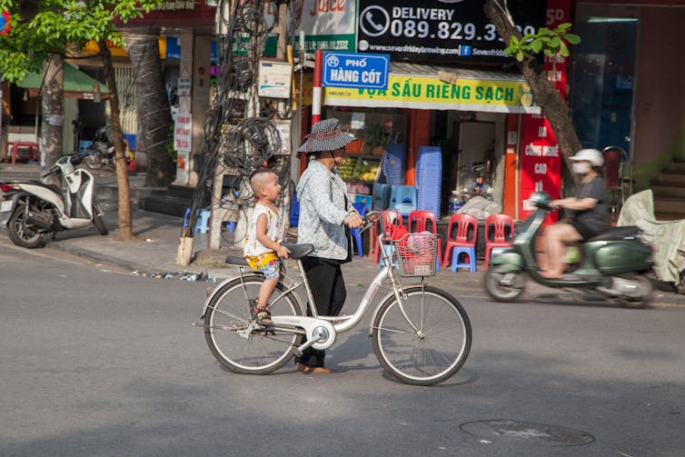 A woman pushes a bike with a small child down a city street.