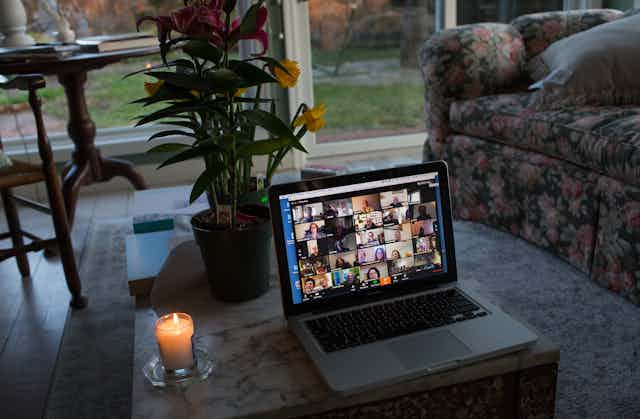 A laptop screen, set on a table, showing a zoom gathering of many people.