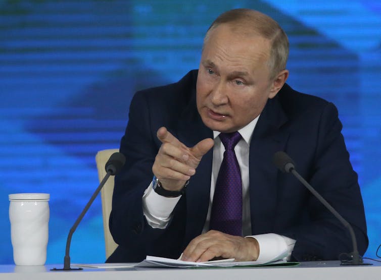 Vladimir Putin sits at a desk.