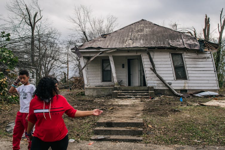 A woman and teenager stand outside a damaged house.