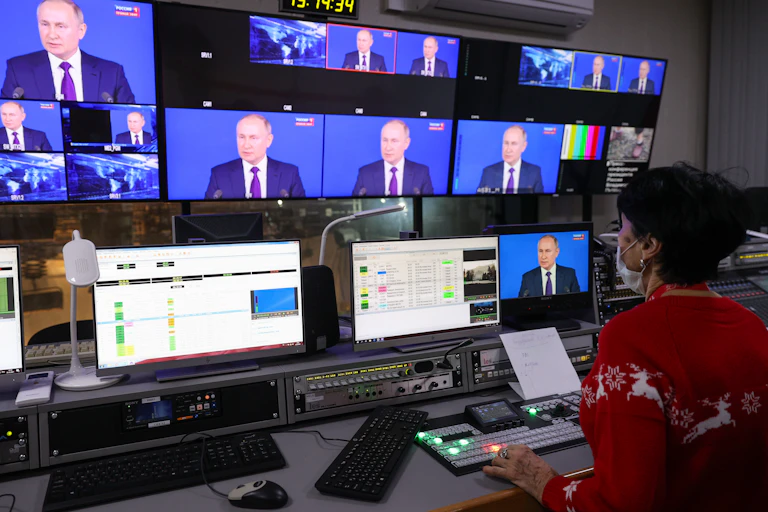 A woman sits facing a series of TV screens all showing Putin's face