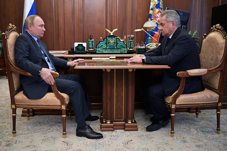 Russian president, Vladimir Putin, sits across a table from defence minister Sergei Shoigu