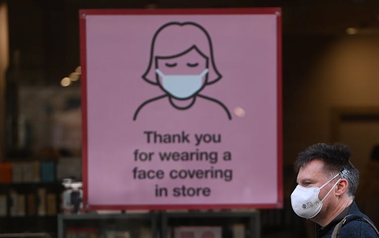 A sign in a shop window asking customers to wear a mask