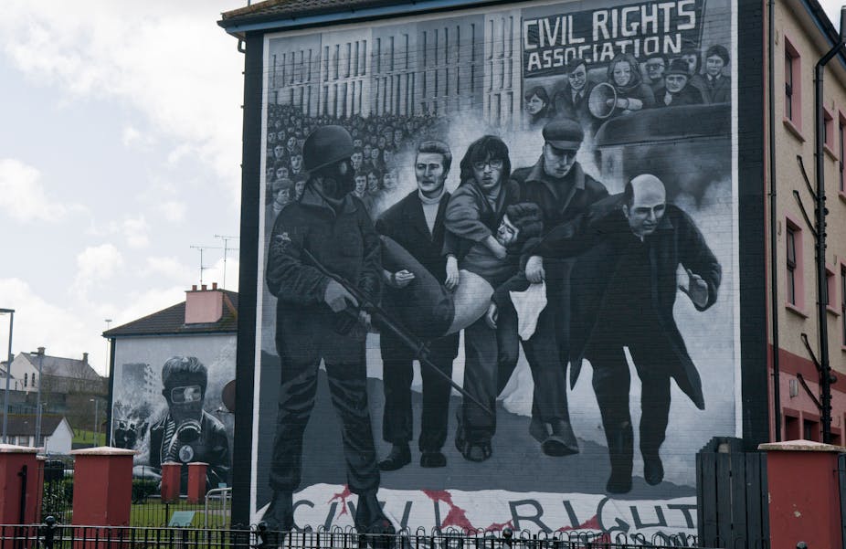 A mural depicts in black and white the iconic photograph of Father Daly waving a white handkerchief and accompanying a group of men carrying a body