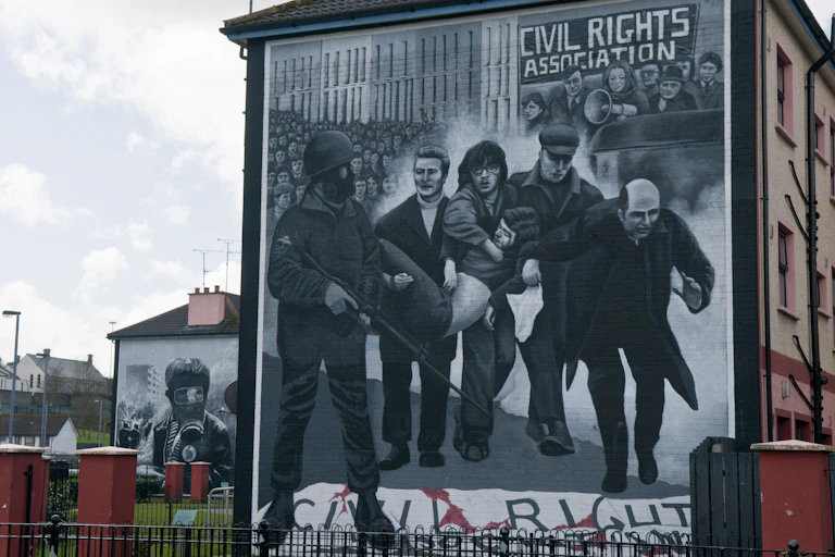 A mural depicts in black and white the iconic photograph of Father Daly waving a white handkerchief and accompanying a group of men carrying a body
