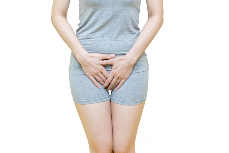 Una mujer con ropa deportiva ceñida se tapa el pubis con las manos.