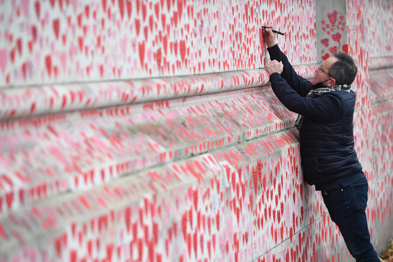A man drawing a heart on the COVID Memorial Wall