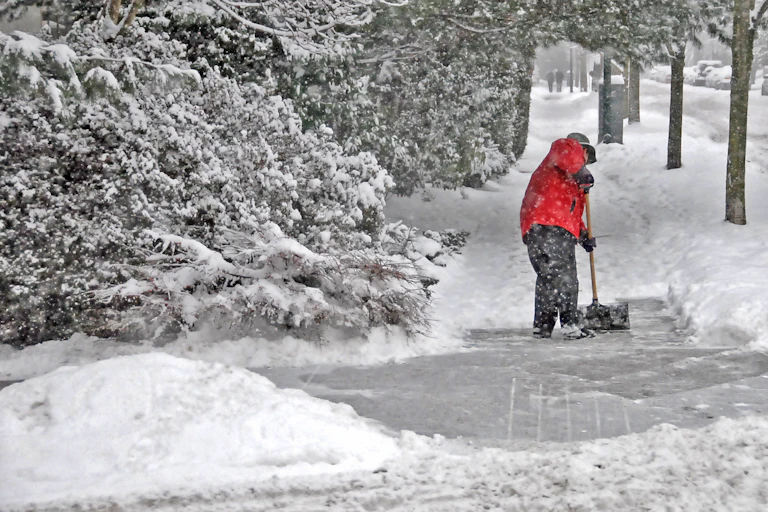 person in snow gear shovels sidewalk while snow falls
