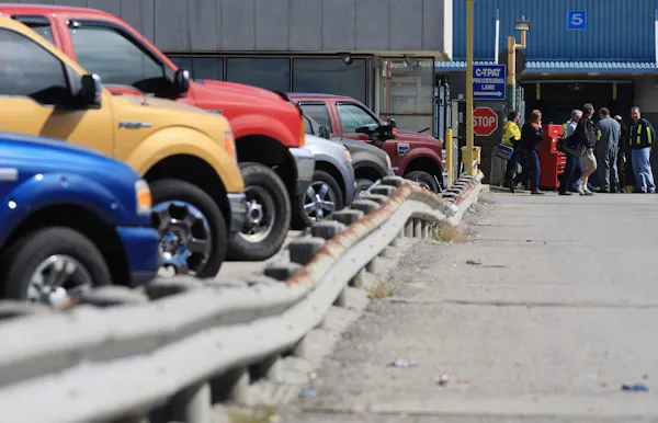 On voit des gens quitter une usine d’assemblage automobile avec une rangée de voitures colorées au premier plan