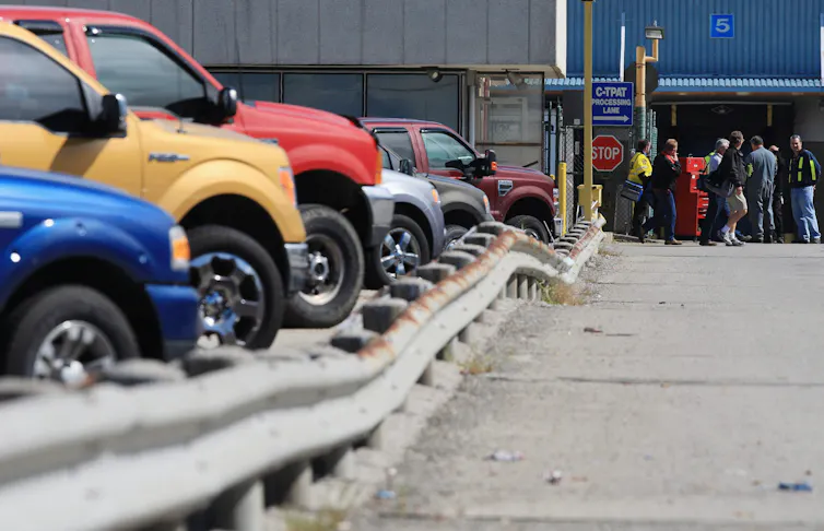 People are seen leaving an auto assembly plant with a row of colourful cars in the foreground.