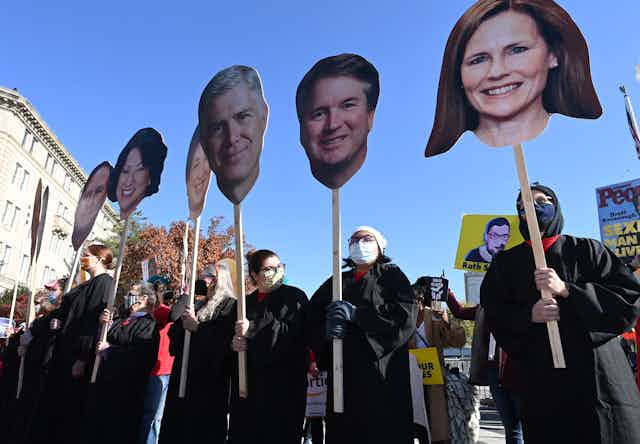 Protesters dressed in black line up holding up large cutouts of Supreme Court justices' heads 