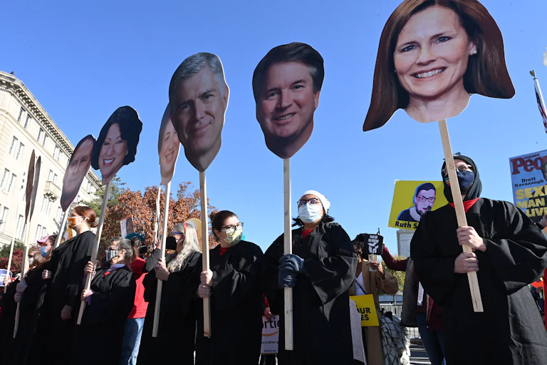 Protesters dressed in black line up holding up large cutouts of Supreme Court justices' heads