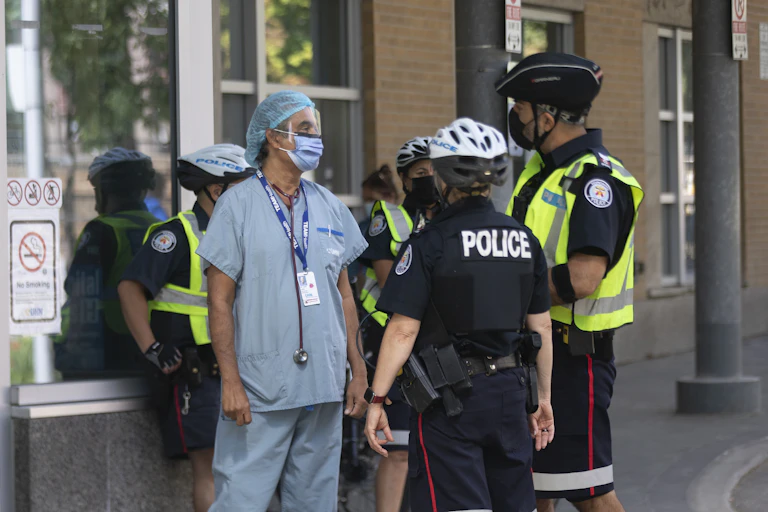 A health-care worker in blue scrubs standing outside with several uniformed police officers