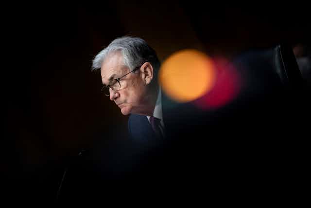 Jerome Powell is seen looking to the side as light flash circles appear next to his face against a black background