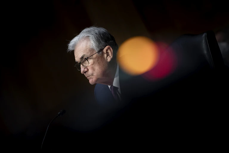 Jerome Powell is seen looking to the side as light flash circles appear next to his face against a black background