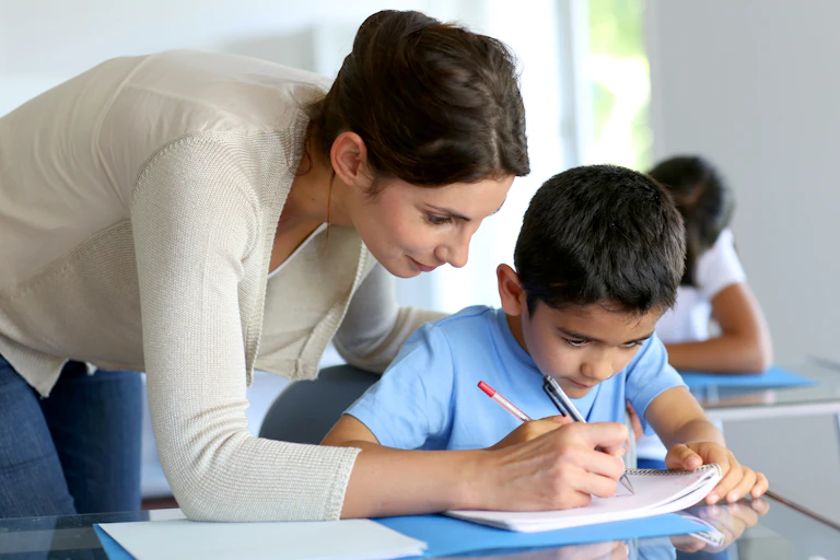 Teacher bending over student's desk to help him with work
