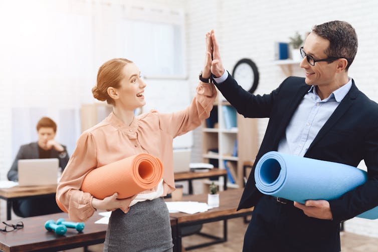 Smiling man and woman holding yoga mats high-five each other