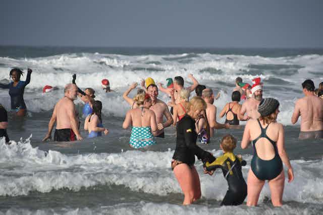 People swimming in the Cornish sea mostly wearing swimming costumes, some wearing a wetsuit