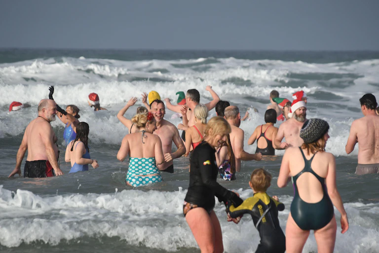 People swimming in the Cornish sea mostly wearing swimming costumes, some wearing a wetsuit