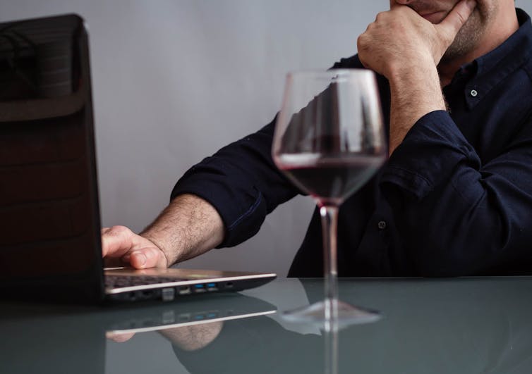 Man working on laptop drinking a glass of wine