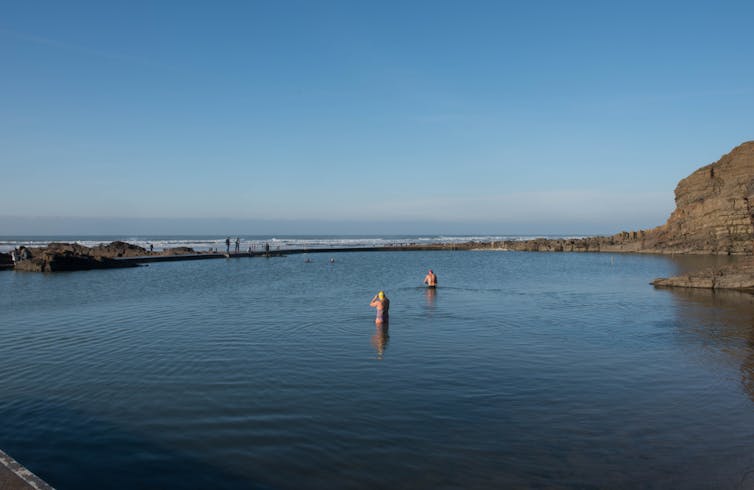 Two swimmers heading out to sea on a sunny day.