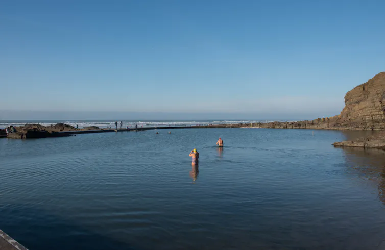 Two swimmers heading out to sea on a sunny day.