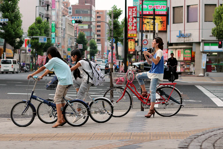 Three female cyclists wait at a road crossing.