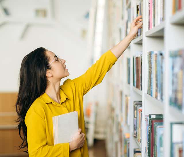 Female student reaching for book in library