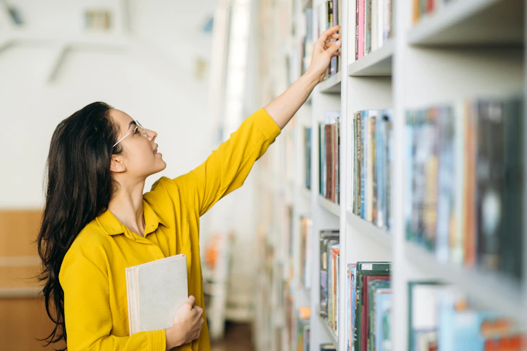 Female student reaching for book in library
