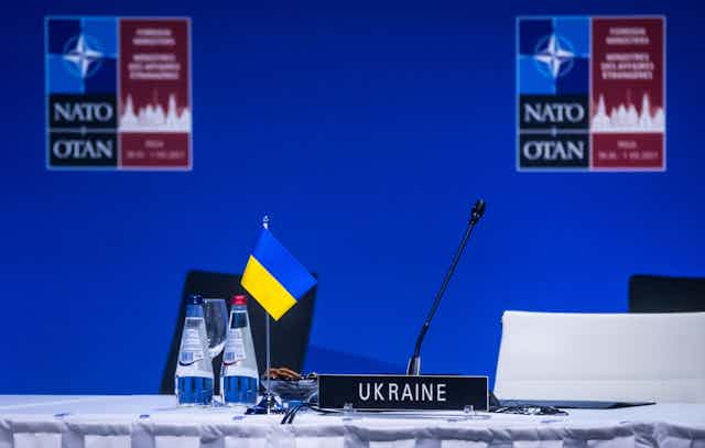 A Ukrainian flag and sign that says Ukraine sit in front of an empty white chair at a NATO meeting