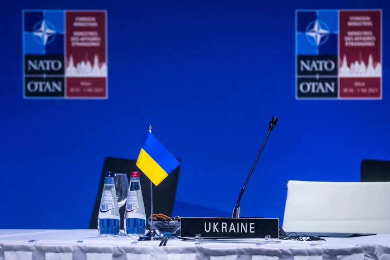A Ukrainian flag and sign that says Ukraine sit in front of an empty white chair at a NATO meeting