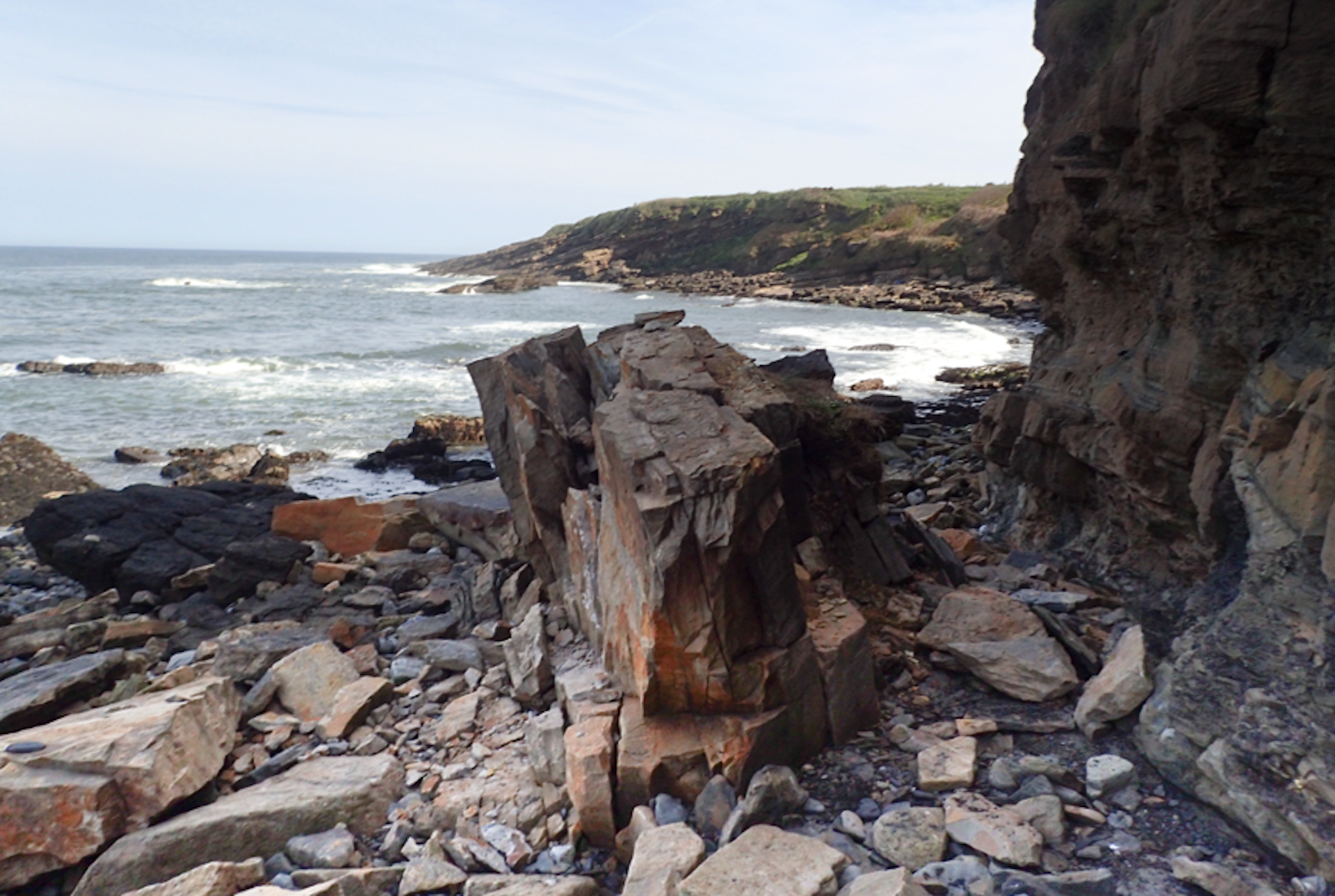 Large sandstone coloured block of rock sitting on the rocky coastline