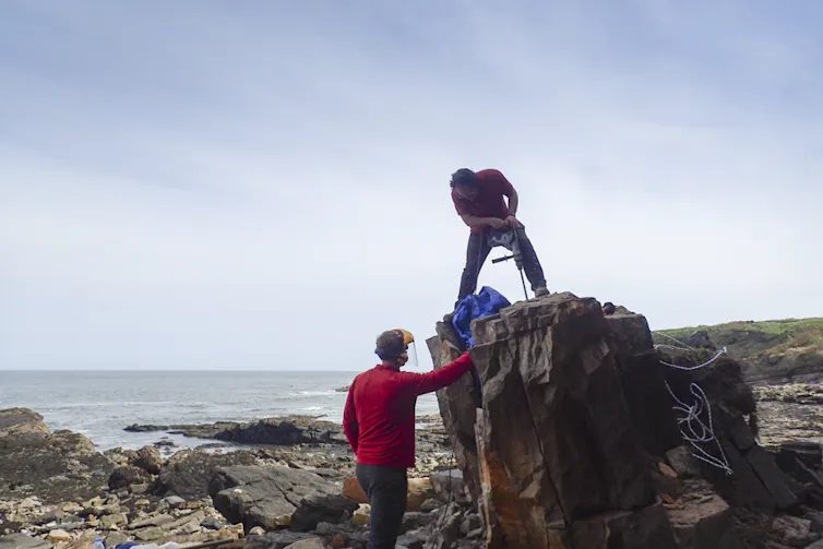 One man standing on the huge block of rock while using a drill to extract the fossil