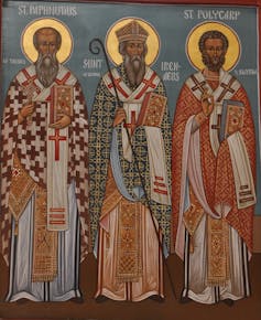 Three saints stand in an icon image, with golden halos around their heads.