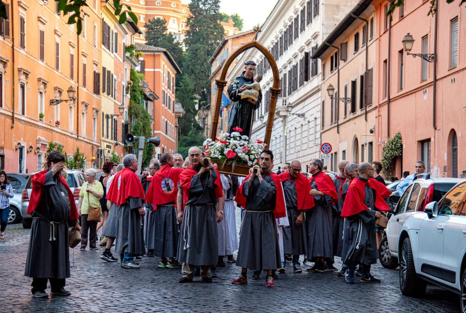 Men wearing cloaks carry a statue of a saint through an Italian street.