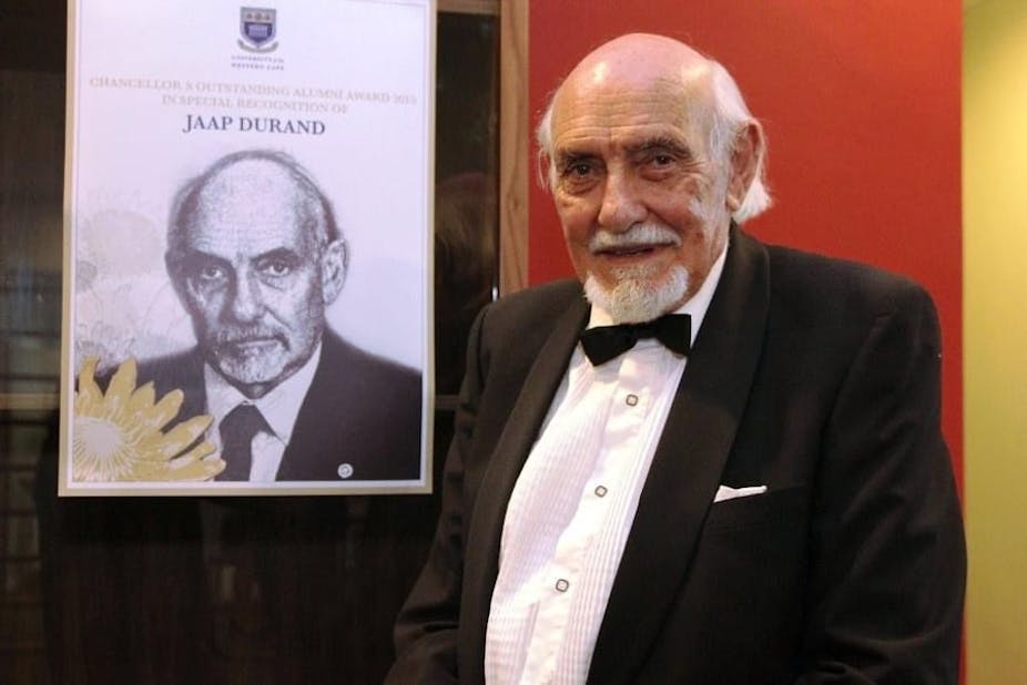 An elderly man in formal wear, standing next to a portrait of himself.