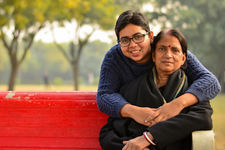 A young South Asian woman hugging an older South Asian woman on a red park bench