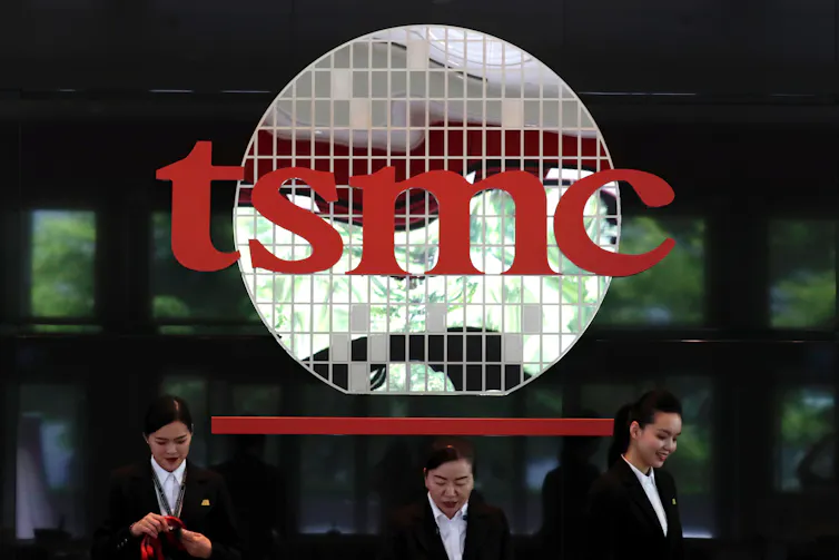Three women with mobile phones walking under a TSMC sign