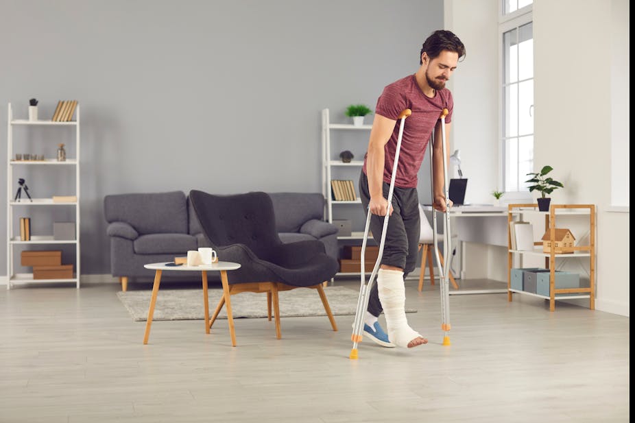 A man with a broken leg walks in his lounge with the use of crutches.