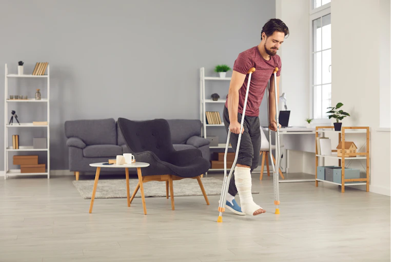 A man with a broken leg walks in his lounge with the use of crutches.