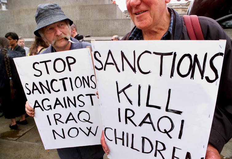 Protesters hold up banners against sanctions against Iraq.